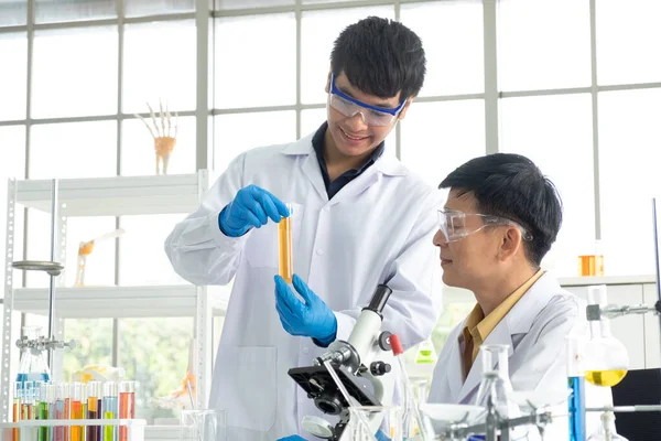 Science, Chemistry, Technology, Biology and Laboratory concept - Asian junior scientist is showing experimental results in test tube to Asian Senior scientist.