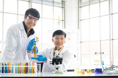 Bilim, Kimya, Teknoloji, Biyoloji ve Laboratuar Konsepti - Asyalı kıdemli ve kıdemsiz bilim adamlarının mutluluk portresi deney tüpünde deneysel sonuçlarını gösteriyor.