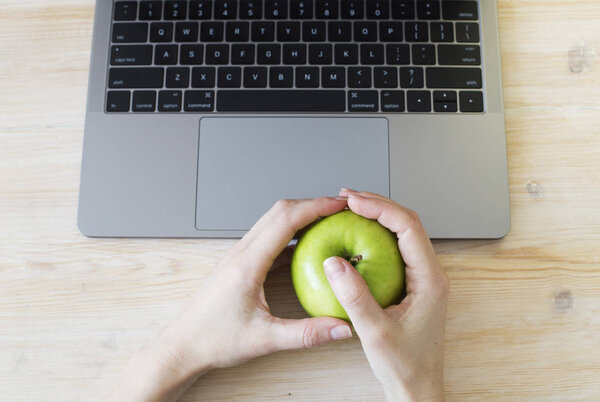 Руки держат зеленое яблоко возле ноутбука
