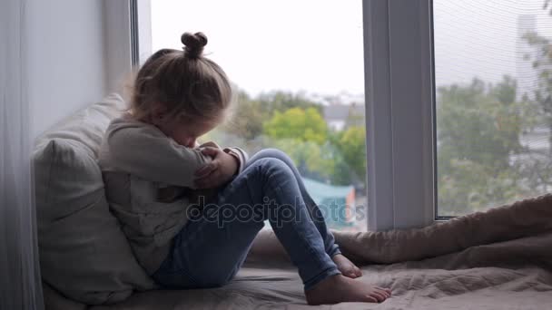 Menina bonito com brinquedo sentado em uma soleira da janela — Vídeo de Stock