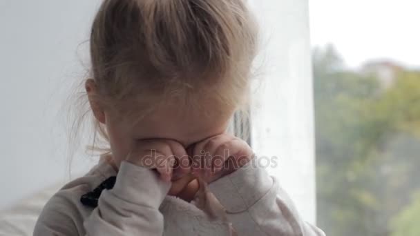 Chica joven se frota los ojos sentado cerca de la ventana — Vídeos de Stock