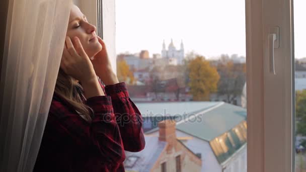 Hermosa mujer frotando sus sienes cerca de la ventana — Vídeos de Stock