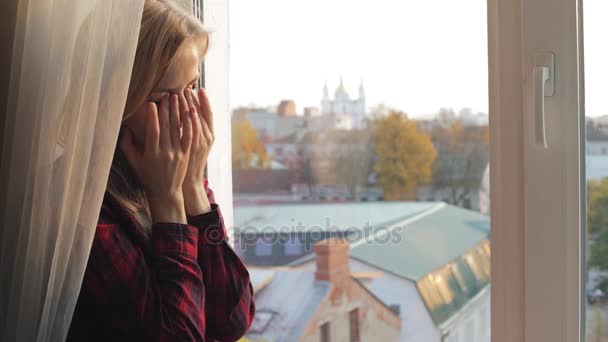 Mulher bonita esfrega seus olhos secos perto da janela — Vídeo de Stock
