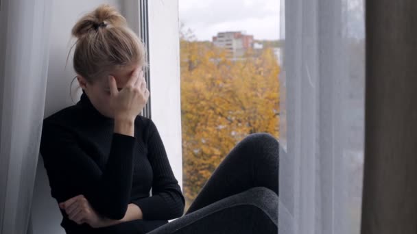 Pencere kenarında oturan genç depresif ve üzgün kadın — Stok video