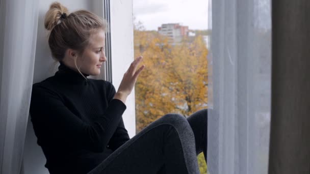 Triste jeune femme assise sur le rebord de la fenêtre et regardant la fenêtre — Video