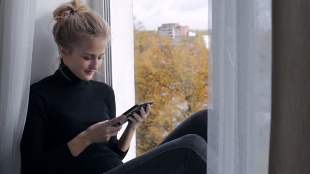 美しい女性を読み取る電子書籍窓辺に座って — ストック動画