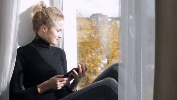 Woman with e-book sitting on the windowsill — Stock Video