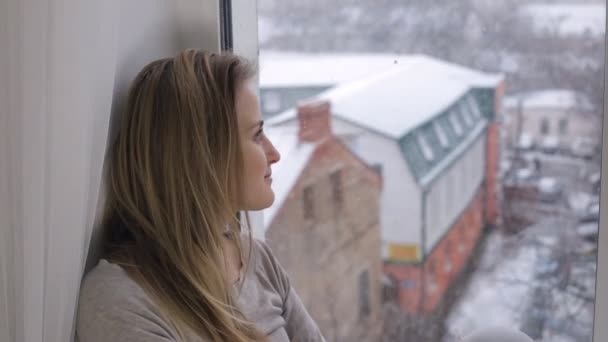 Soñando chica mirando a través de la ventana en las nevadas — Vídeo de stock