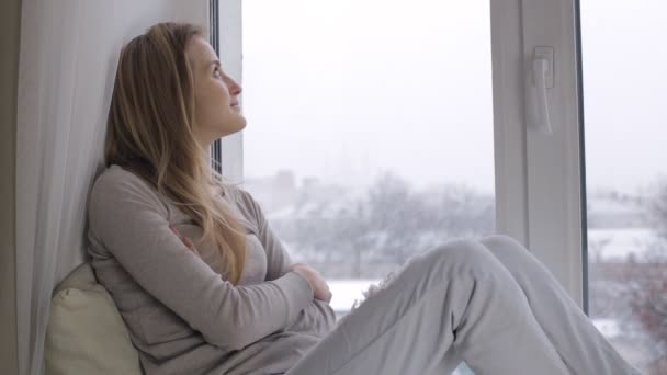 Девушка смотрит в окно на снегопад — стоковое видео