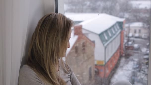 Vrouw Zoek op sneeuwval door uit het raam — Stockvideo