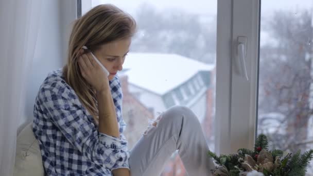 Νεαρή γυναίκα που μιλάει στο τηλέφωνο από το παράθυρο σε ένα windowsill — Αρχείο Βίντεο