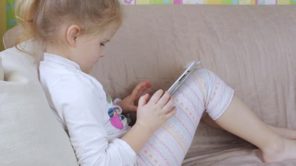 Jeune fille mignonne avec tablette à la maison. Fille à l'aide d'une tablette couchée sur le canapé — Video