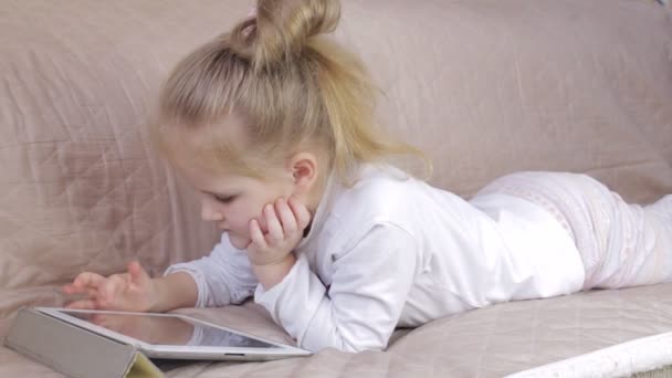 Мила молода дівчина лежить на дивані і використовує цифровий планшет. Дівчина з планшетом вдома — стокове відео