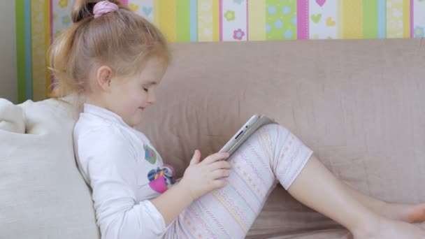 Молодая девушка на диване с планшетным компьютером дома — стоковое видео