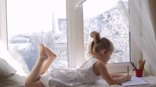 Carino bambina disegna con matite colorate. Ragazza si trova sul davanzale della finestra — Video Stock