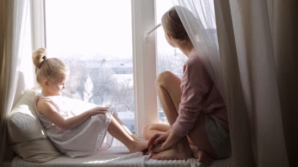 Mamá y su hija están sentadas en un alféizar de la ventana. Familia feliz — Vídeo de stock