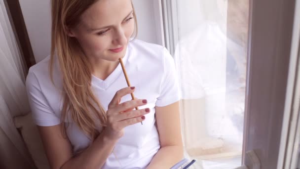 Vrouw zitten op een vensterbank en schrijft in haar dagboek of tijdschrift — Stockvideo