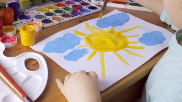 Cute young girl draws yellow sun and blue clouds. Painting concept — Stock Video
