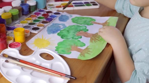 Cute girl painting brown trees with green leaves on white paper — Stock Video