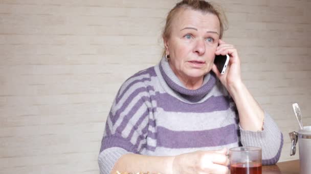 Mutfak masasına oturan telefonda konuşurken büyükanne — Stok video