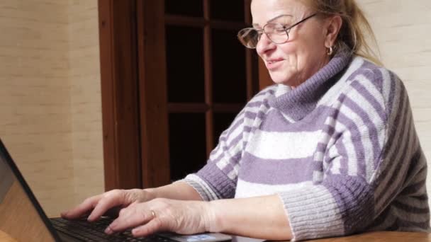 Mormor arbetar på en bärbar dator sitter vid bord. Farmor med dator — Stockvideo