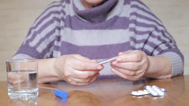 Oudere vrouw met een thermometer in handen — Stockvideo