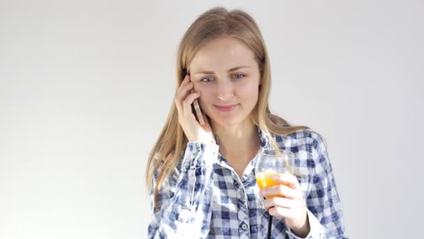 Mujer joven con un vaso de jugo habla en el teléfono móvil — Vídeos de Stock