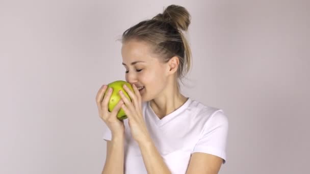 Muchacha joven atractiva muerde una gran manzana verde. Levanta el pulgar y sonríe — Vídeo de stock