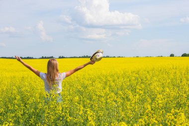 Sarı bir tarlada elini güneşe kaldıran bir kız.