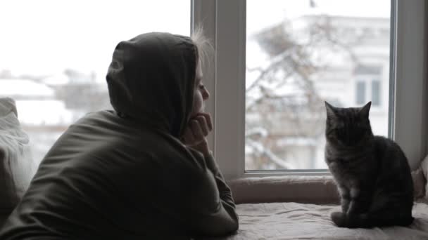 Mädchen schaut aus dem Fenster und träumt, und eine britische Katze sitzt in der Nähe — Stockvideo