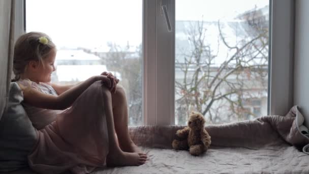 Meisje zittend op een vensterbank met een teddybeer en lachend — Stockvideo