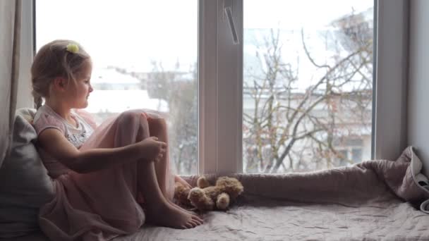 Menina sentada em uma soleira da janela, e brinca com seu brinquedo — Vídeo de Stock