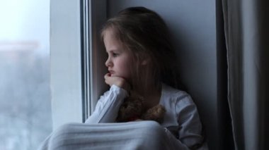 Küçük kızgın ve hoşnutsuz kız pencere eşiğinde oturuyor.
