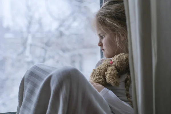 Kind hält Spielzeug in der Hand und schaut aus dem Fenster — Stockfoto