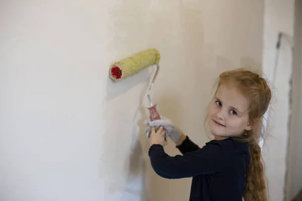 아름다운 소녀는 열심히 흰색으로 벽을 페인트하고 카메라에 분칠을 한다 스톡 이미지