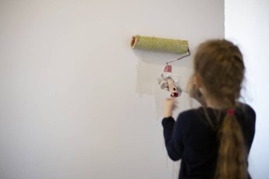 Küçük kız bir anaokulu öğrencisi evin duvarlarını beyaza boyuyor..