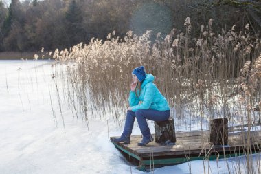 A girl sits on a pier near a frozen lake. The concept of freedom and life outside the city