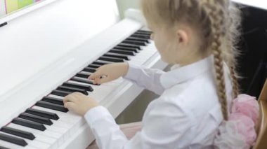 Child plays music on a white piano