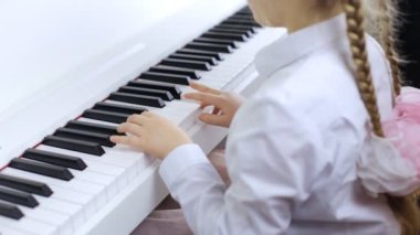 Küçük kız beyaz bir piyanoda klasik müzik çalar.