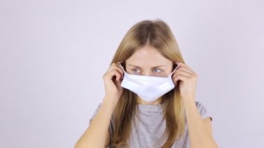 Bir kadın tıbbi maske takıyor ve kameraya bakıyor.