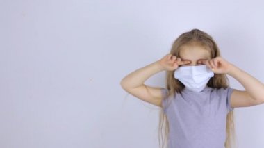 Koruyucu tıbbi maskeli bir çocuk elleriyle gözlerini ovuşturuyor.