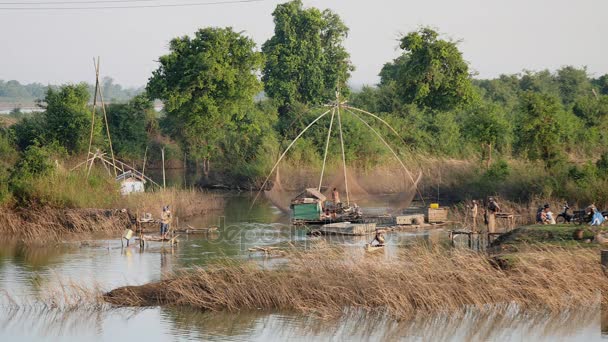 Red de pesca china está cayendo en el agua en el fondo, mientras que los pescadores de pie en pequeñas plataformas de madera en busca de un buen lugar para lanzar la red en primer plano — Vídeos de Stock