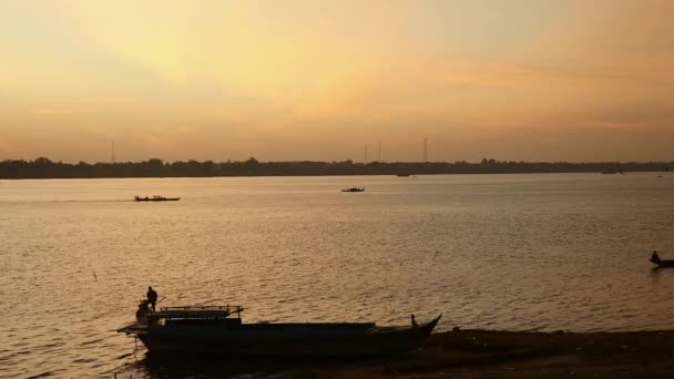 Rybář, pracující při východu slunce v popředí s hejnem ptáků letící nad řekou, lodě, rybaření na řece jako pozadí — Stock video