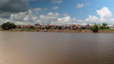 Bulutlu mavi gökyüzü altında düşük gelgit nehir kenarında Köy stilt-evler