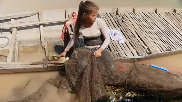 Mujer sacando agua de una canoa dugout mientras sostiene la red de pesca en la orilla del río (de cerca  ) — Vídeos de Stock