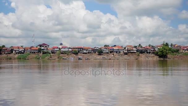 Village stilt-houses on the riverside at low tide under cloudy blue sky (shot from a moving boat) — Stock Video