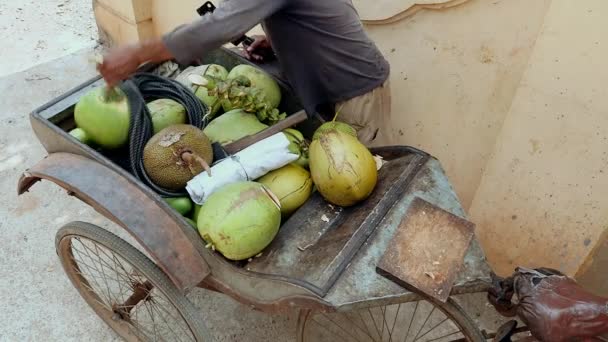 Кокосовый уличный торговец готовит для клиентов кокосовый орех: сверху отрезанный, сверху отверстие и сбоку разрез с соломинкой через него — стоковое видео