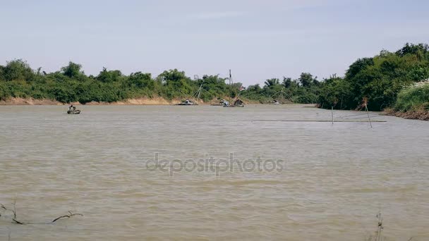 Vue à distance d'une pirogue motorisée sur rivière et péniches avec filets de pêche en toile de fond — Video