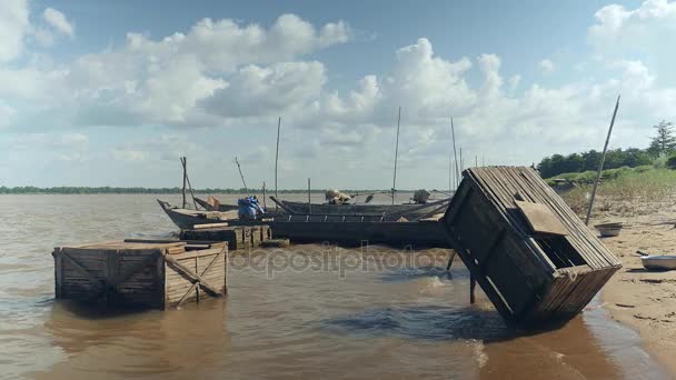 Дерев'яні рибні ящики біля невеликих рибальських човнів на краю річки у вітряний день (закрити  ) — стокове відео