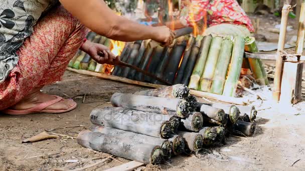 Women turning bamboo cakes cooking on fire — Stock Video